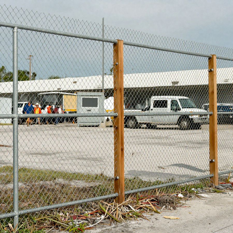 A tall, heavy-gauge commercial chain link perimeter fence around a business property