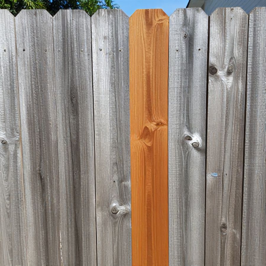 A weathered, graying wood fence board next to a freshly stained section of the same fence