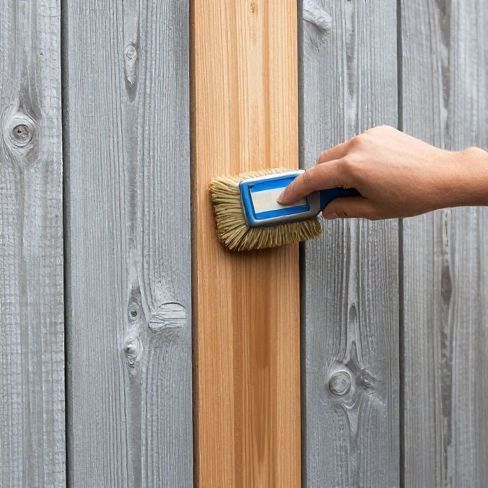 Stain being brushed onto a wood fence board, with untreated boards alongside.