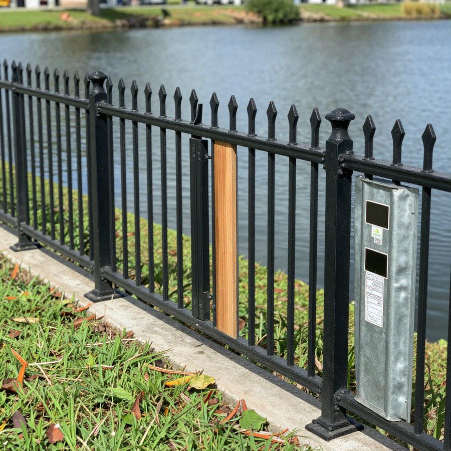 A black aluminum ornamental fence along a waterfront lawn, its open pickets keeping the view